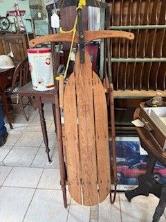 Wooden sled with curved runners, resting in a room, with a yellow rope tied to the front.
