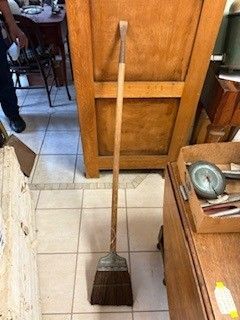Broom standing upright against a wooden cabinet, in a room with a tiled floor and furniture.