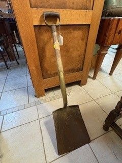 Shovel leaning against wooden cabinet on tiled floor.