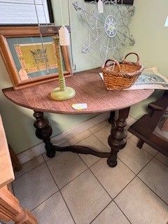 Brown, half-round antique table with turned legs, basket, and lamp on top, in a shop.