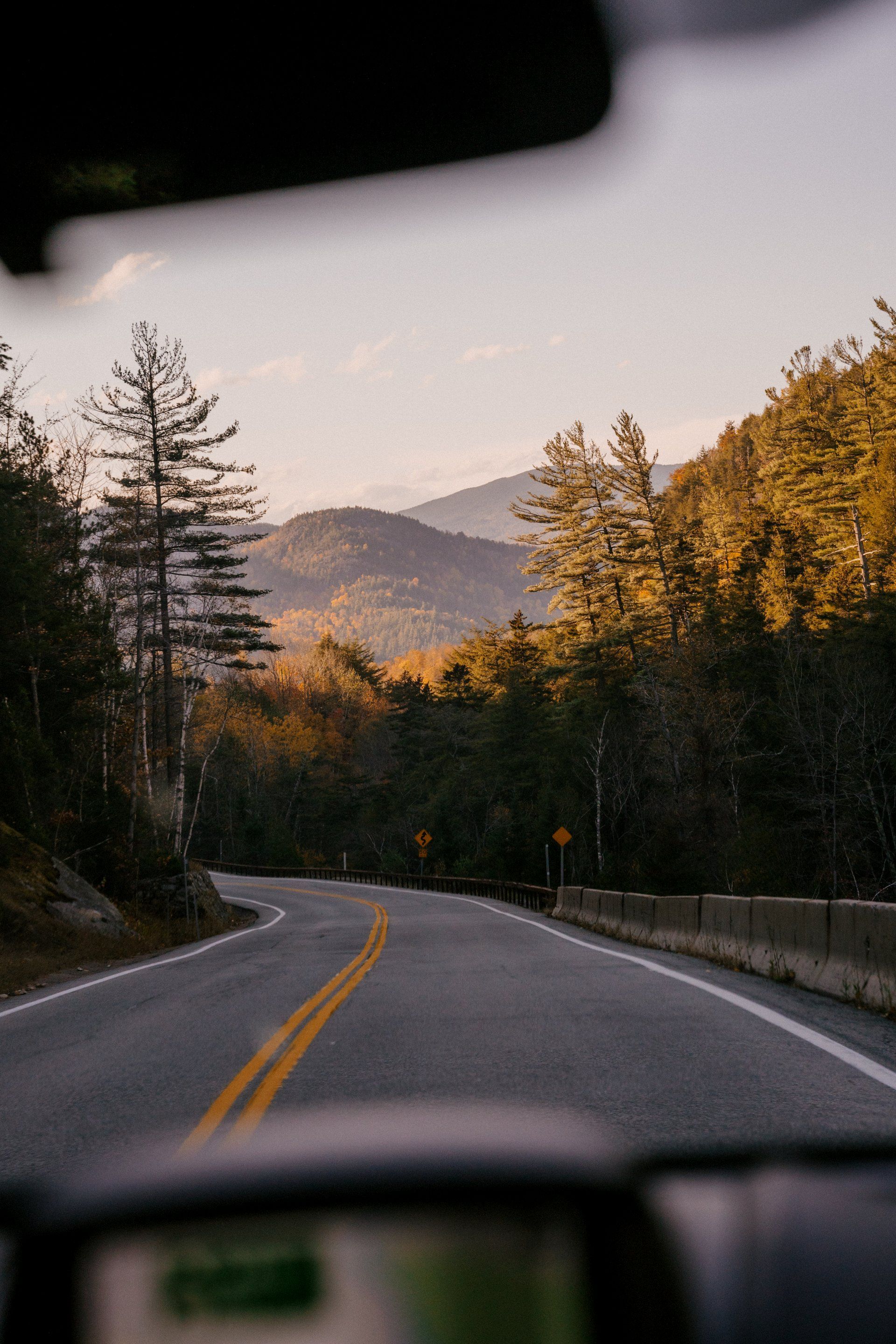 A car is driving down a road with mountains in the background.