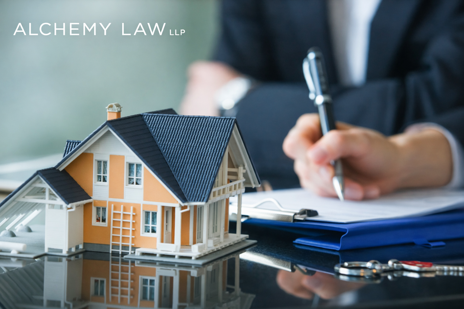 Miniature house next to a person signing documents. A key is also on the table.