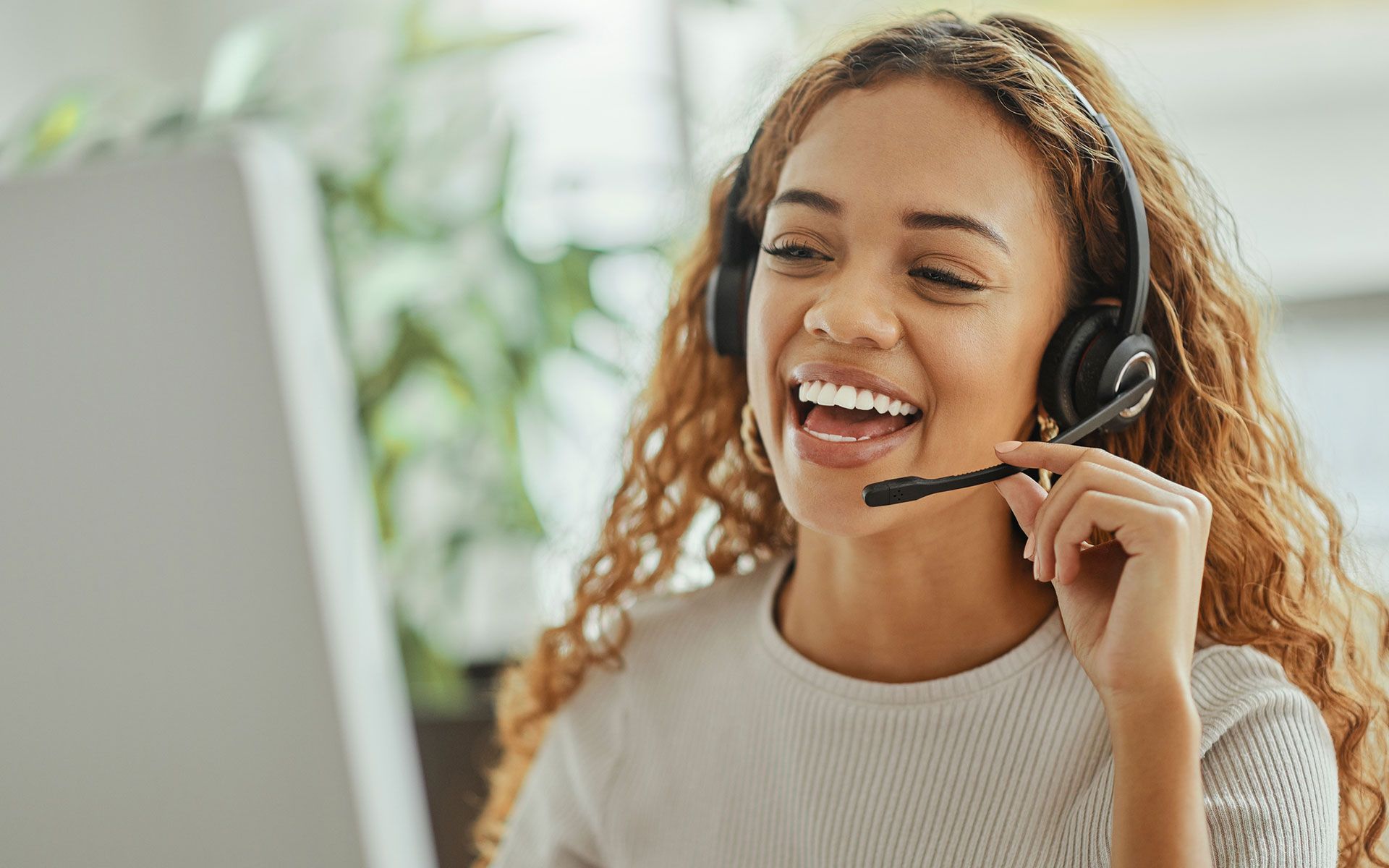 A woman wearing a headset is smiling while talking on a computer.