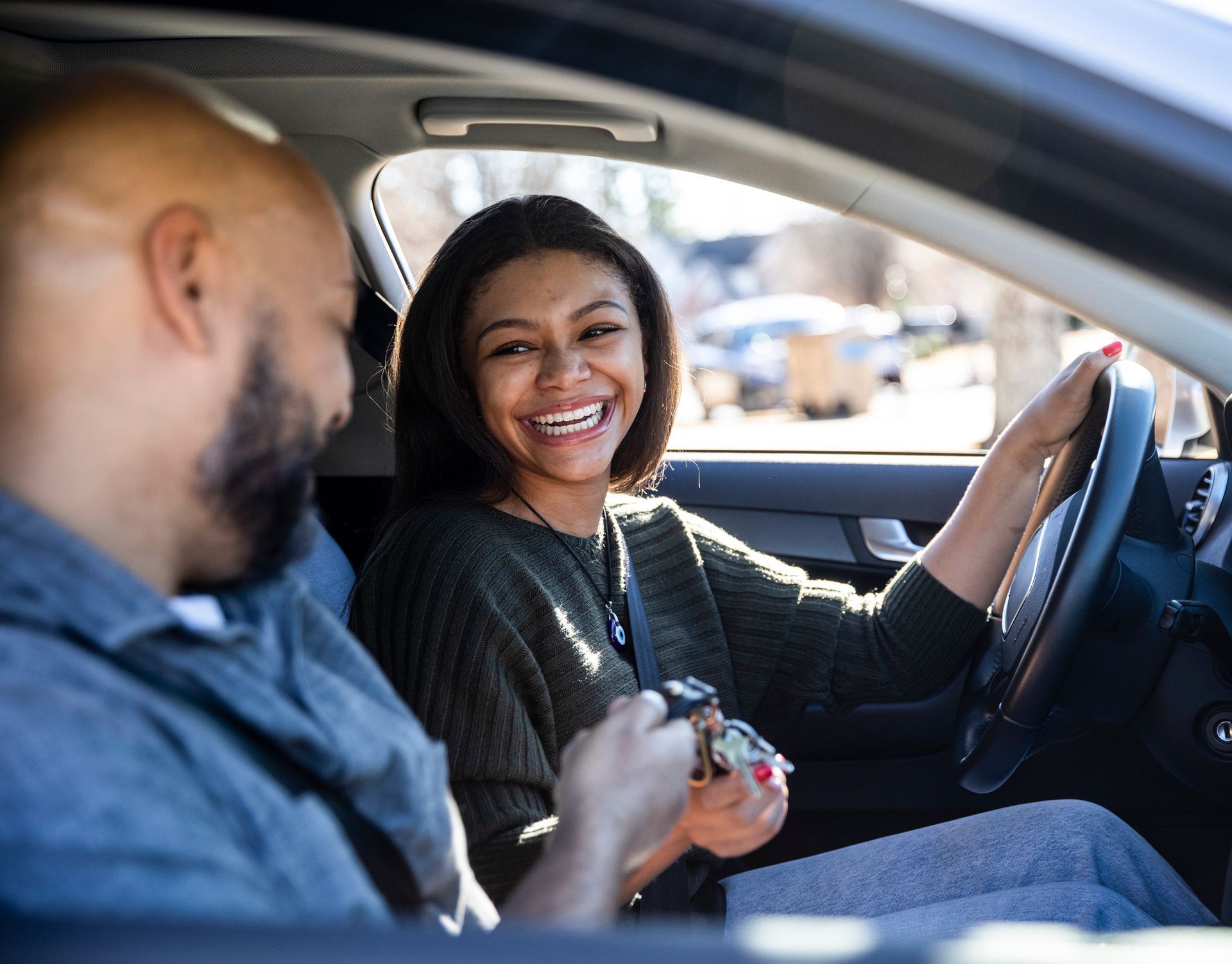 A man and a woman are sitting in a car and the woman is smiling.