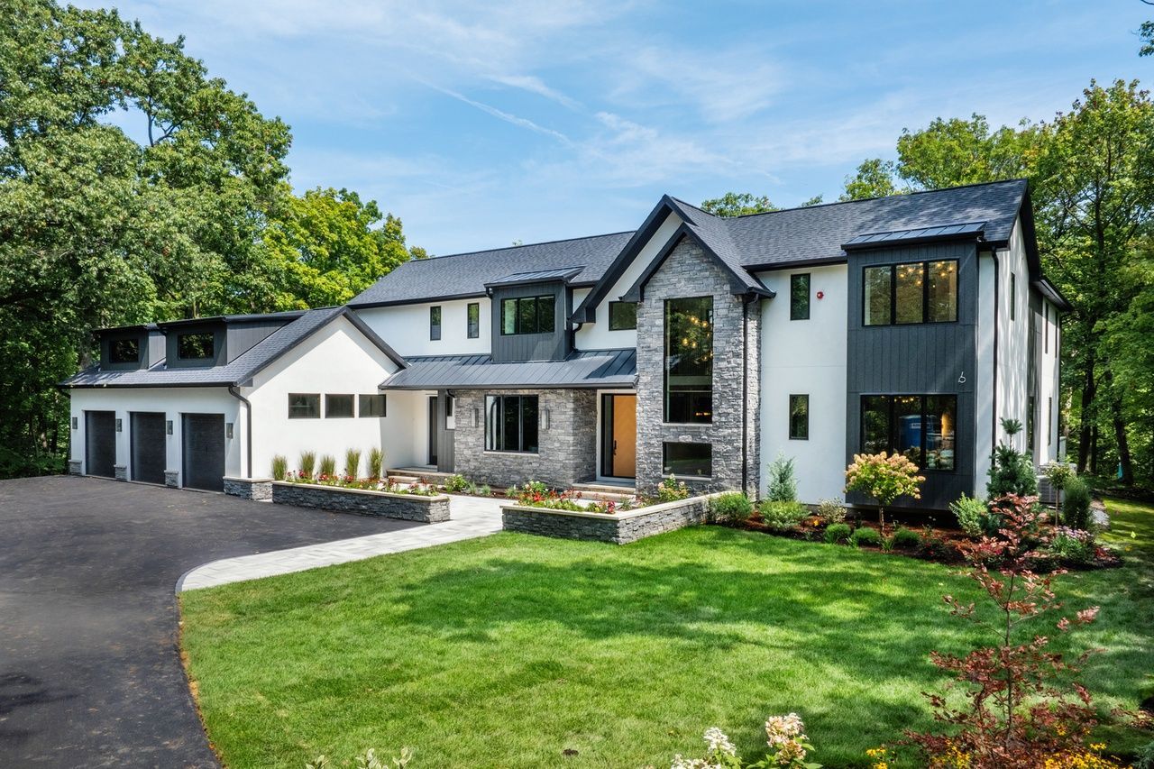 A large white house with a black roof is sitting on top of a lush green lawn.