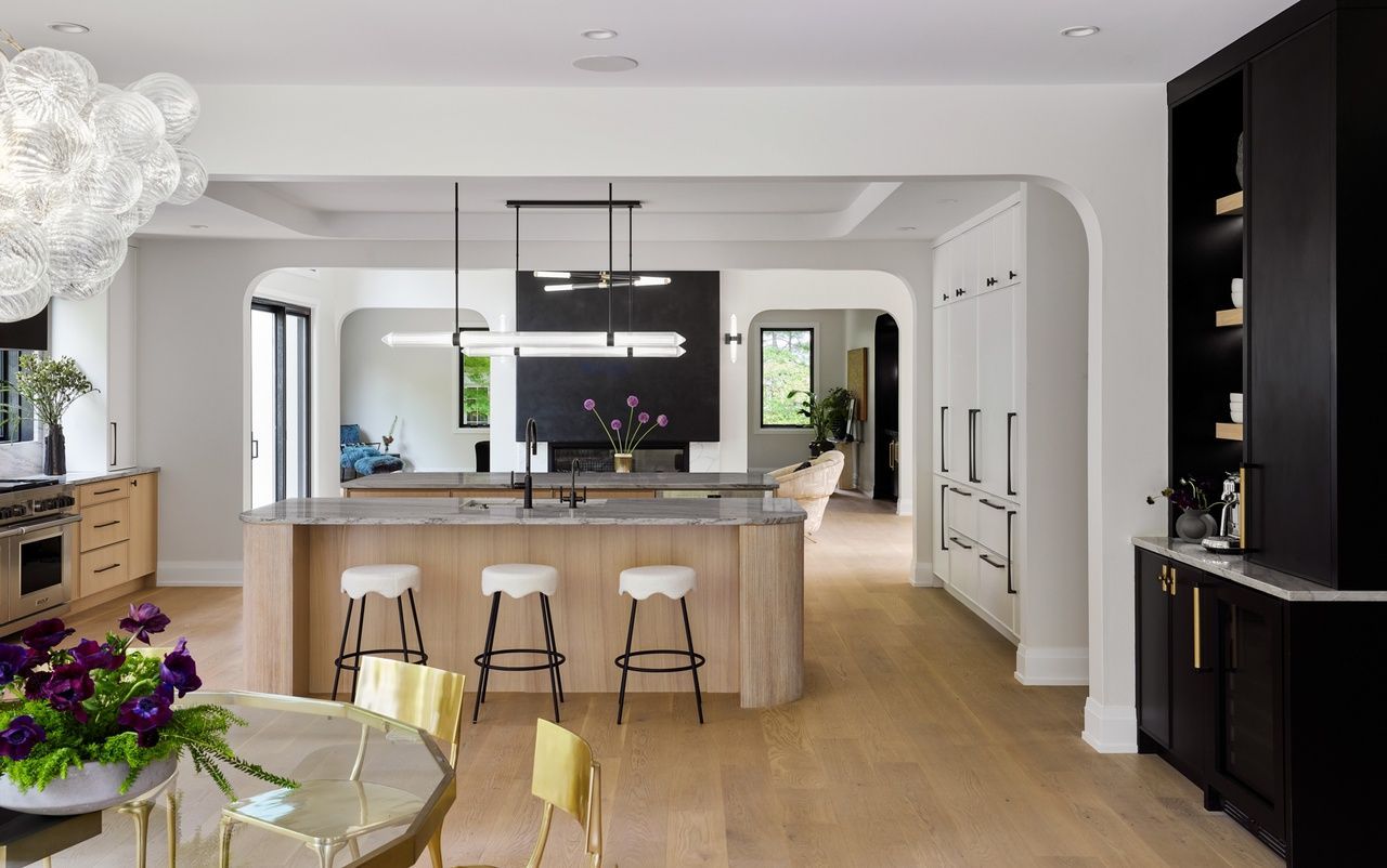 A kitchen with a large island , stools , a table and a chandelier.