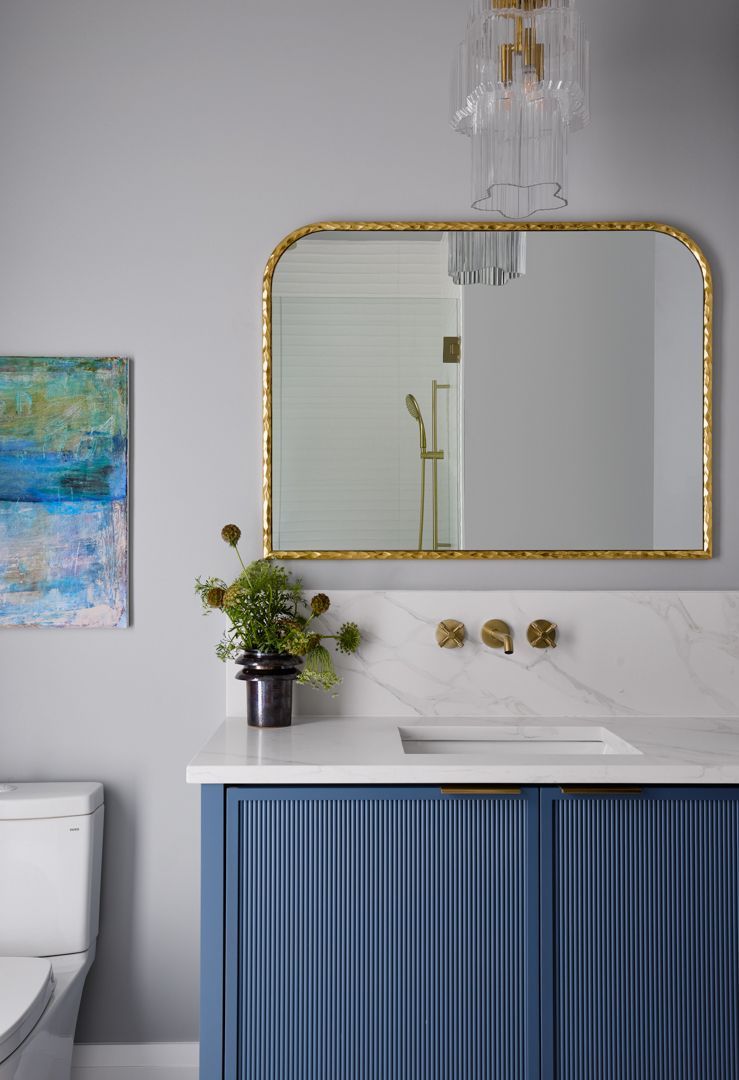 A bathroom with a sink , toilet , mirror and painting on the wall.