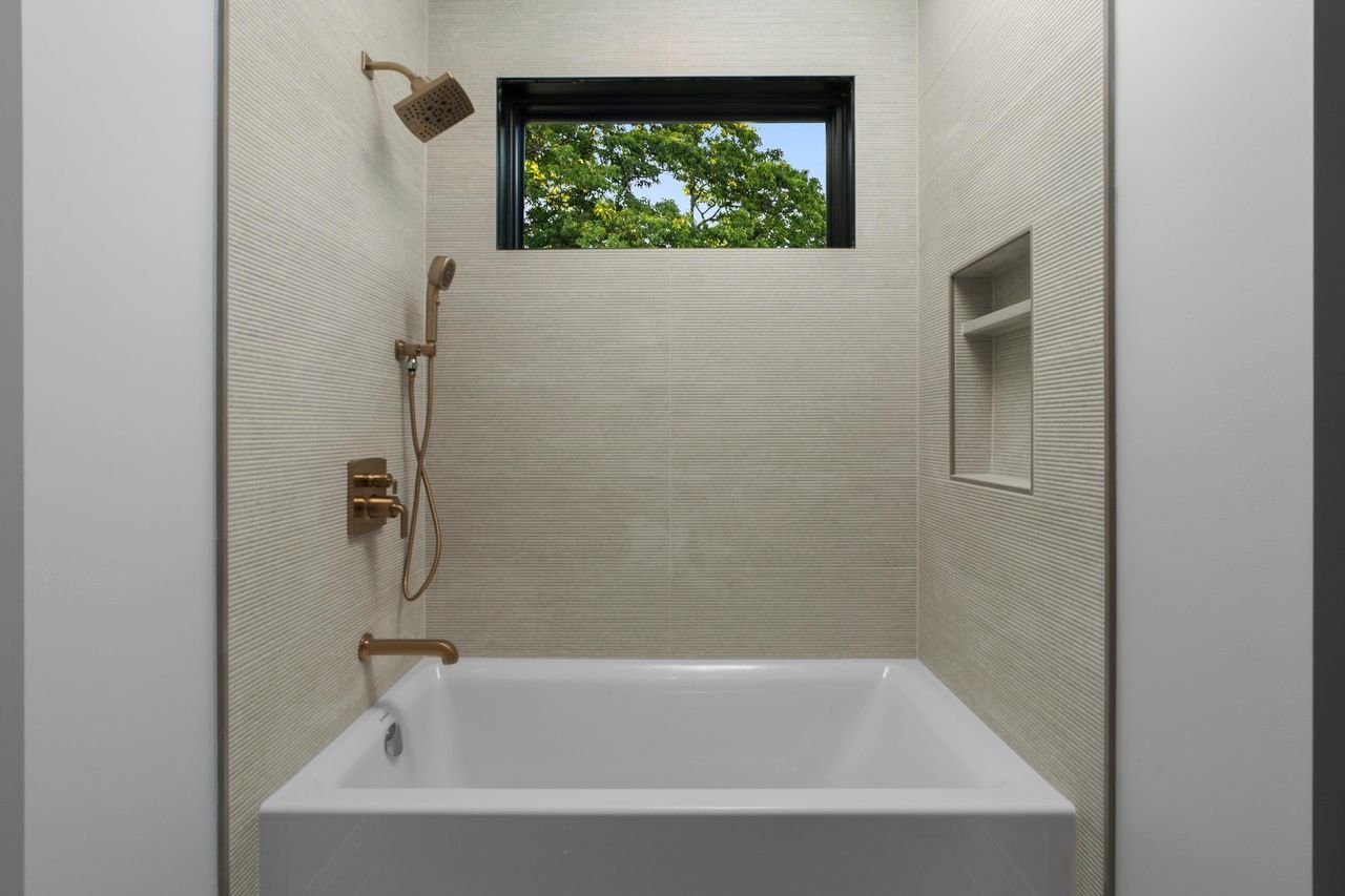 A bathroom with a tub , shower , and window.