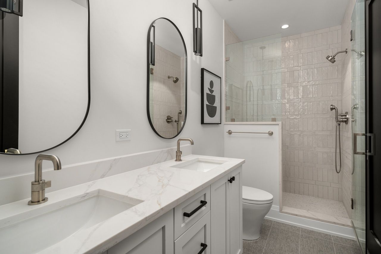 A bathroom with two sinks , a toilet , and a walk in shower.