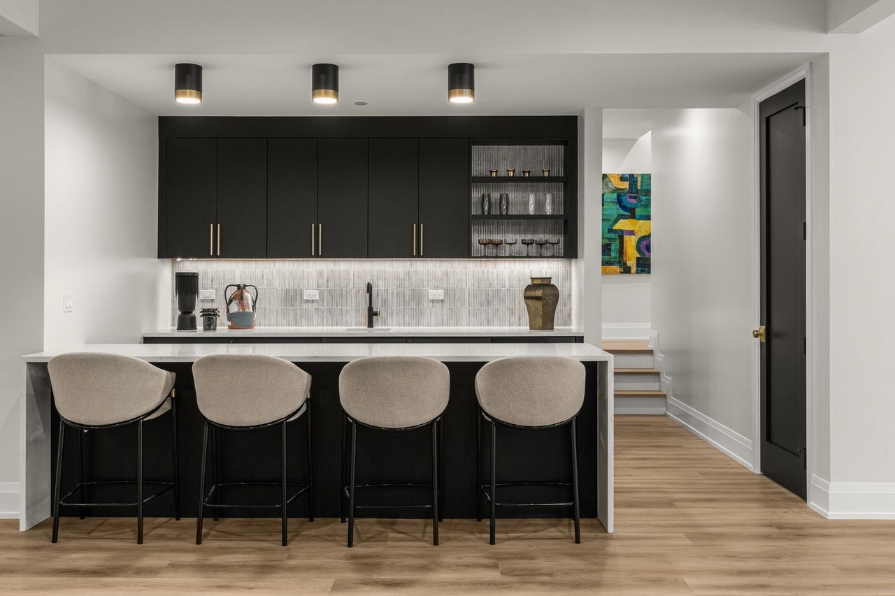 A kitchen with black cabinets and white counter tops and stools.