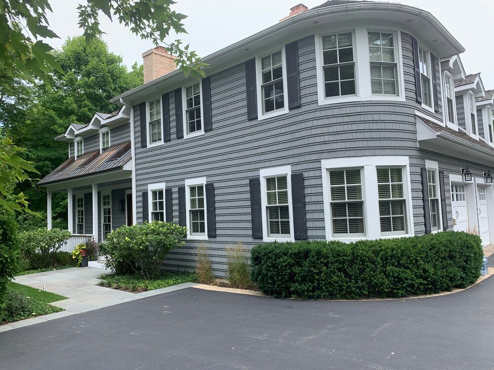 A large gray house with a lot of windows and black shutters.