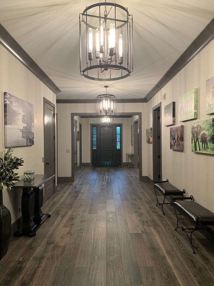 A long hallway with hardwood floors and a chandelier hanging from the ceiling.