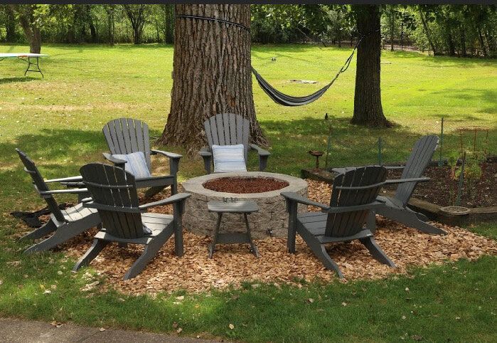 A fire pit is surrounded by chairs and a hammock.