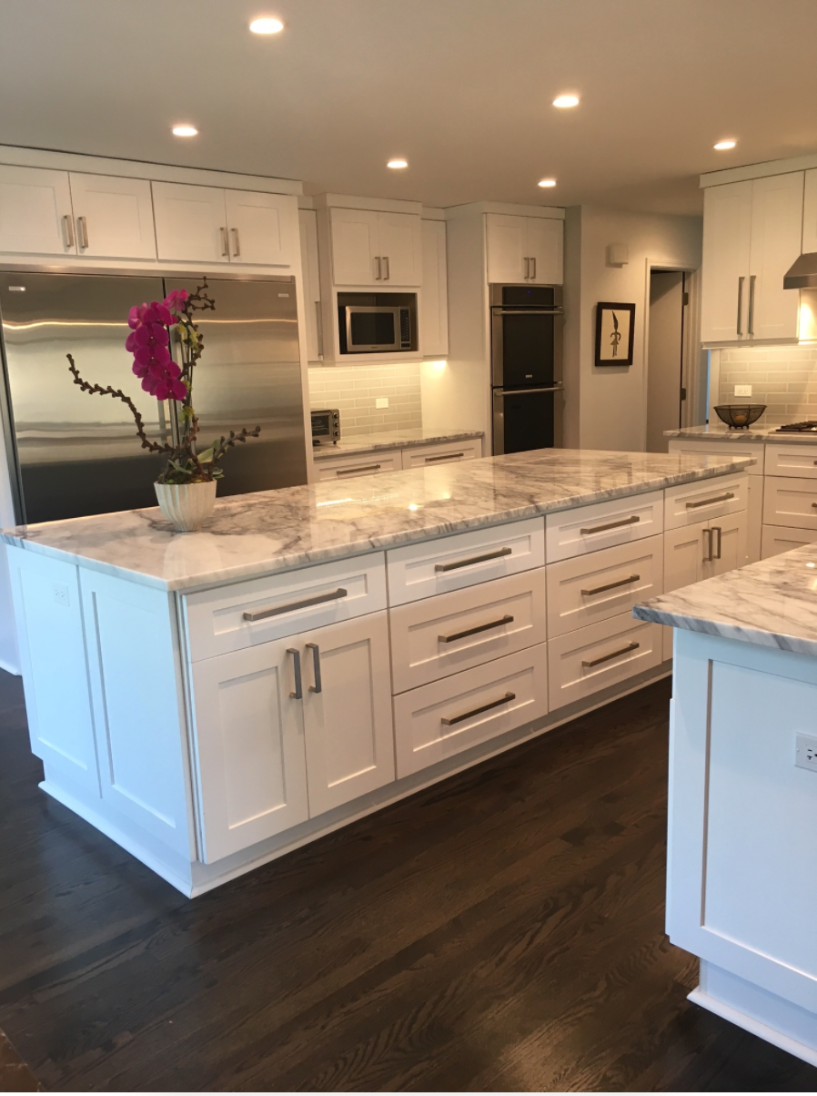 A kitchen with white cabinets and marble counter tops