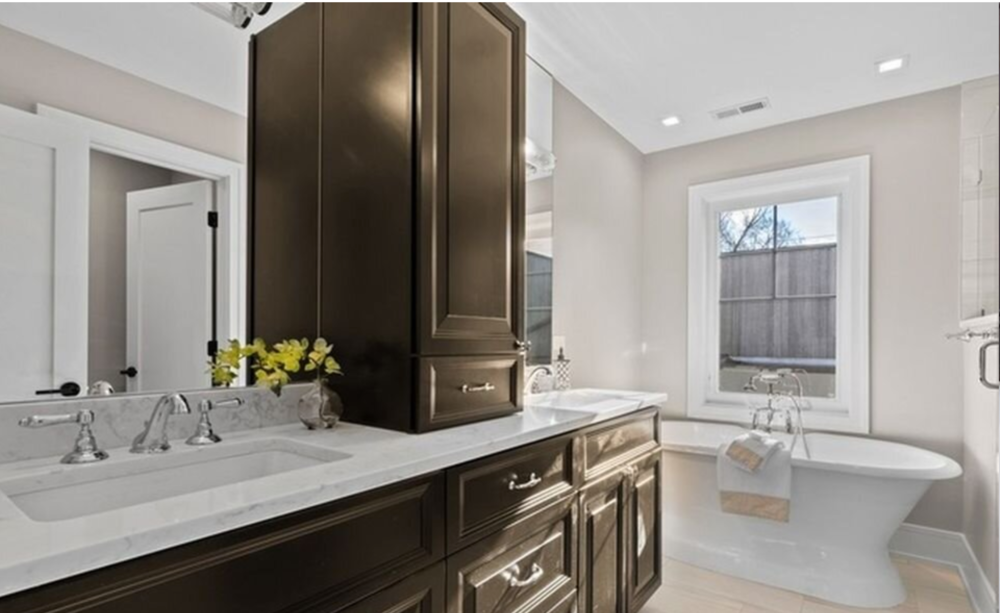 A bathroom with two sinks , a tub , a mirror and a window.