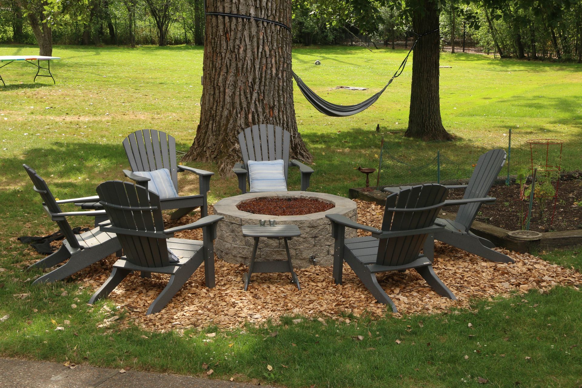 A fire pit is surrounded by chairs and a hammock.
