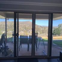 Sliding glass doors open onto a patio with a dining set, overlooking a grassy landscape with distant hills under a blue sky.