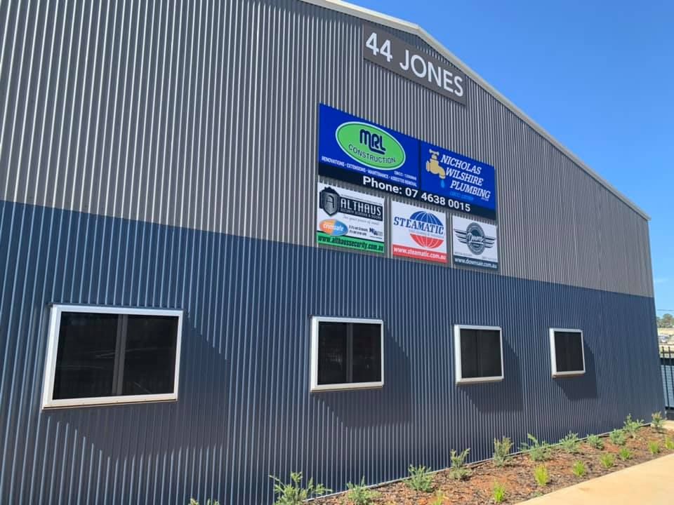 Exterior of a grey, corrugated metal industrial building at 44 Jones with several business signs and windows.