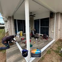 A worker installing security screens on an outdoor patio floor with tools and materials scattered nearby.