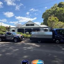 Two work trucks parked in front of a white building with a dark roof under a sunny blue sky.