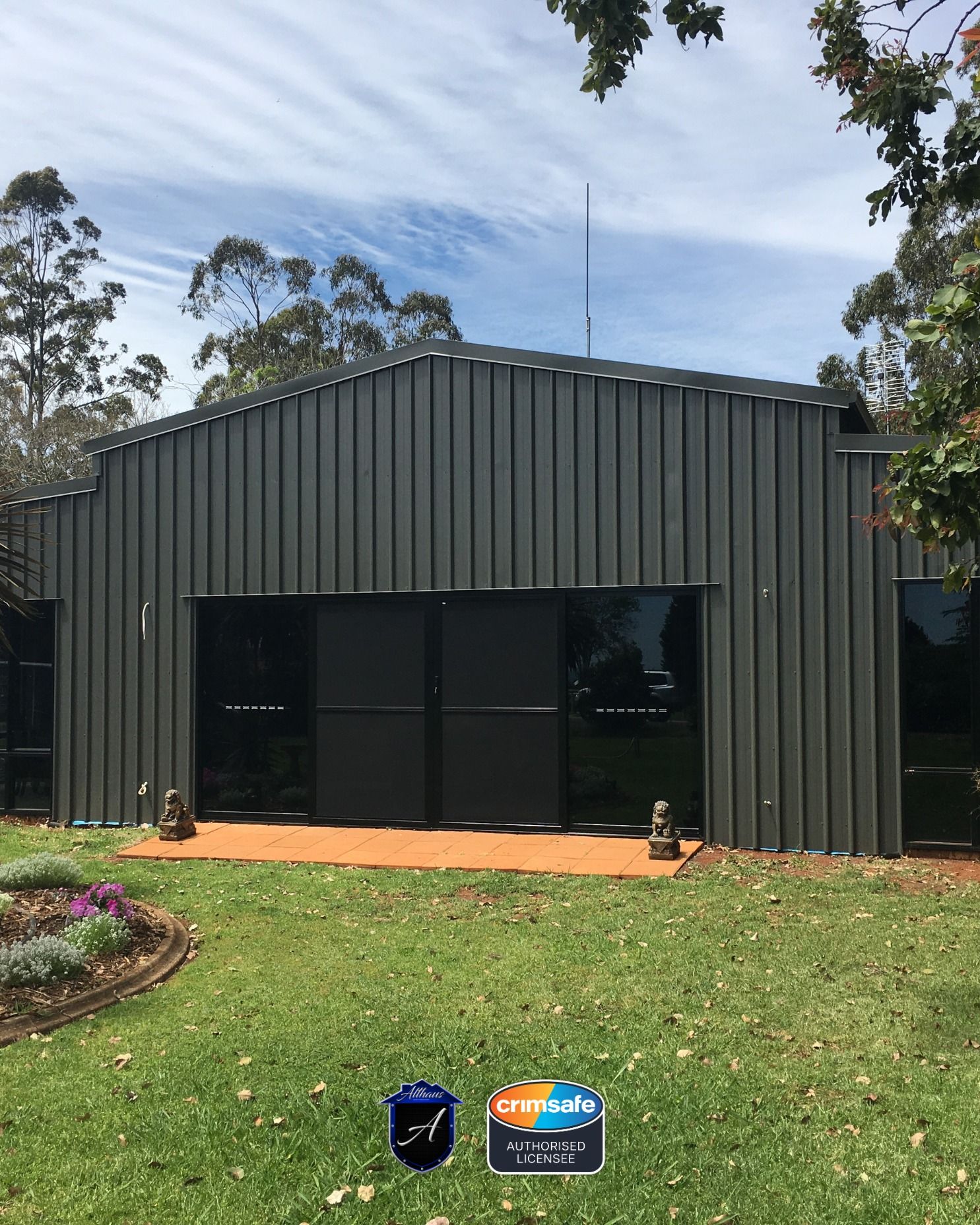 A dark gray, metal-sided building with large black glass doors and a small orange front stoop, set in a grassy yard.