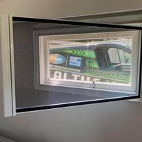 A white-framed retractable window screen installed over a window that shows a green van parked outside.