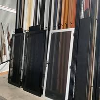 A rack displaying multiple door and window screen samples in various colors and finishes inside a warehouse.