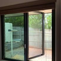 A view through a partially open dark-framed glass door looking out onto a backyard with a fence and a drying rack.