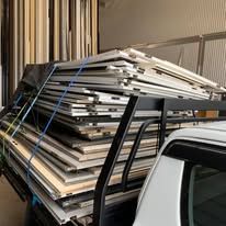 A stack of rectangular panels secured with blue straps on a truck's flatbed rack inside a building.