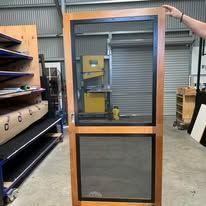 A wooden door frame with two black mesh screens, being held up in a workshop setting.