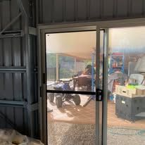A sliding glass door viewed from inside a shed, looking out to a patio with a blue quad bike and outdoor items.