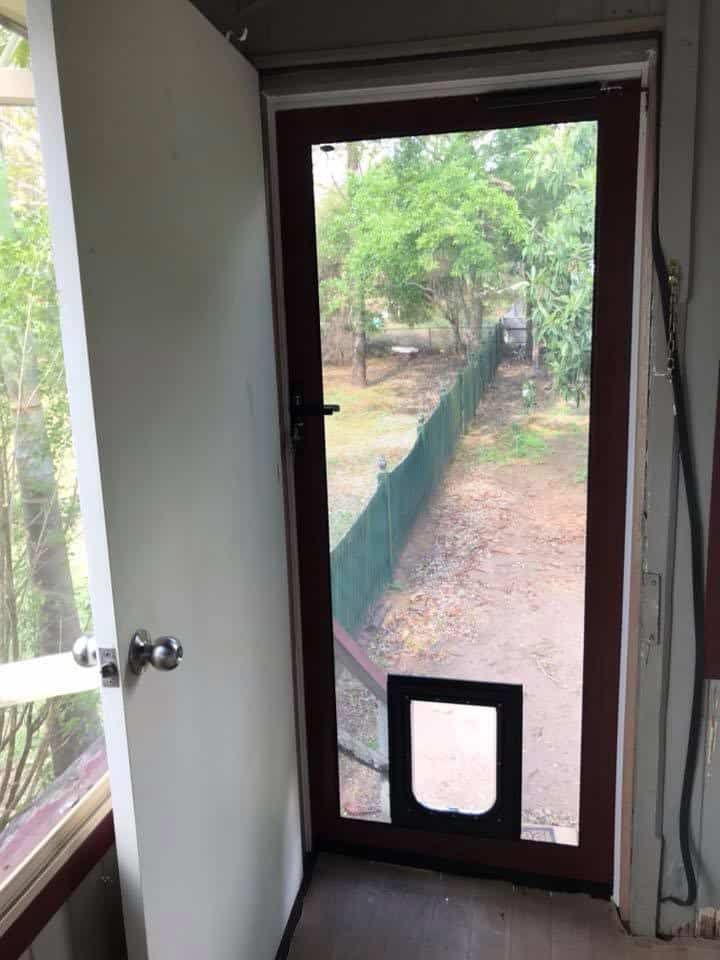 An open white door reveals a brown screen door with a pet door installed at the bottom, looking out to a fenced yard. An open white door reveals a brown screen door with a pet door installed at the bottom, looking out to a fenced yard.