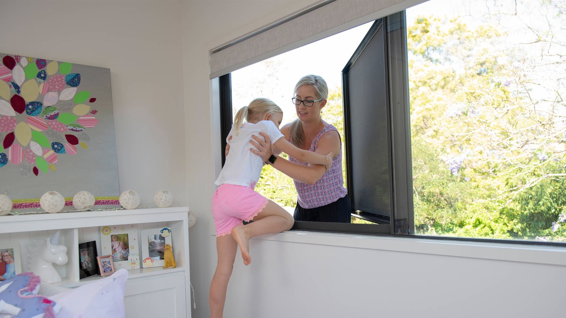 Woman helping child climb through open window in a bright room