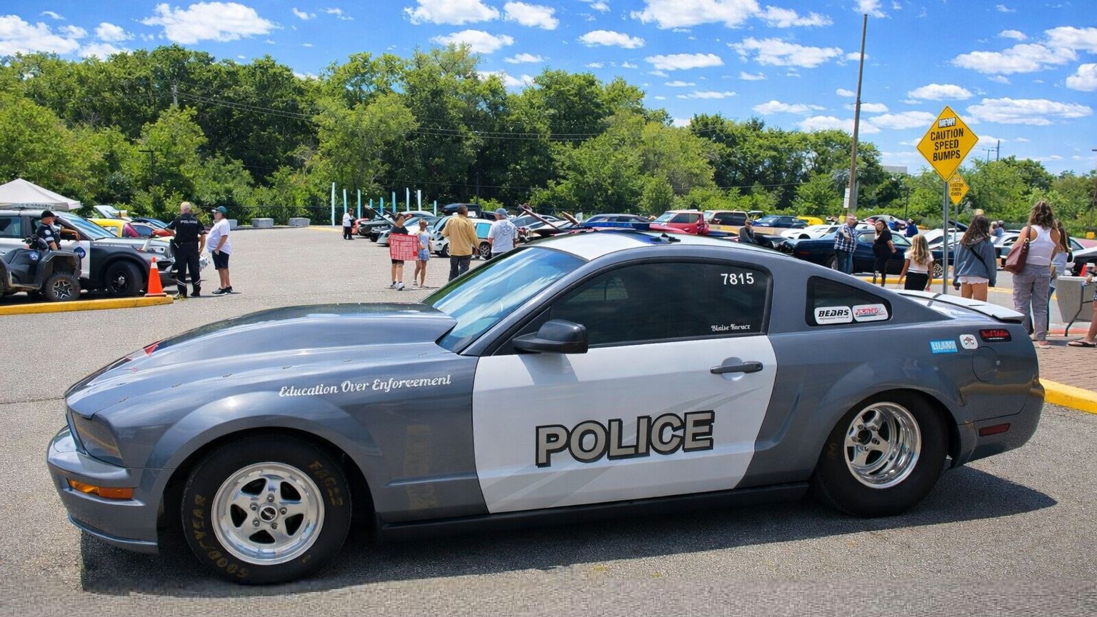 A gray and white Ford Mustang police car parked in a paved parking lot on a sunny day.