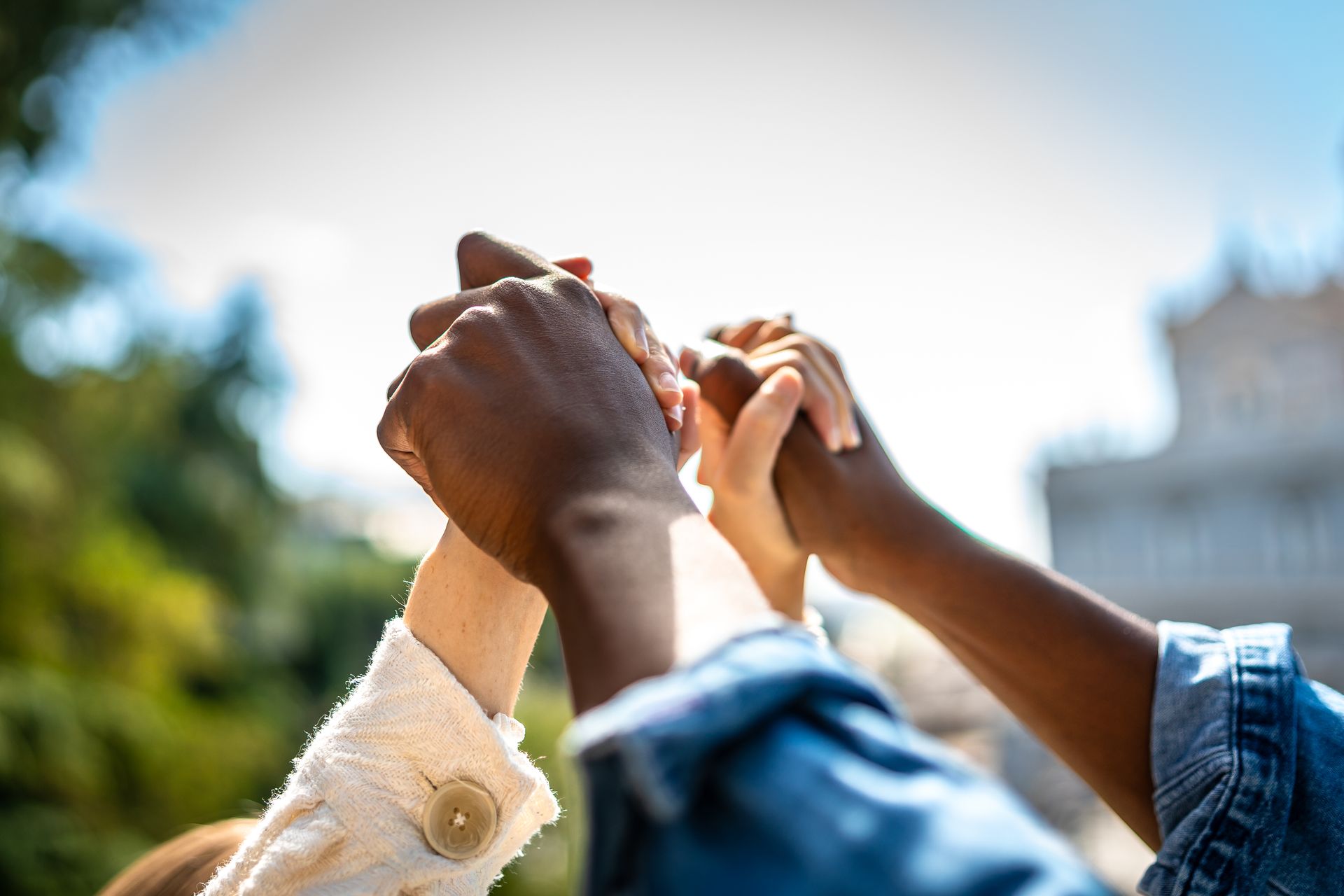 Close-up of several people holding hands raised high against a blurred outdoor background, symbolizing unity and support.