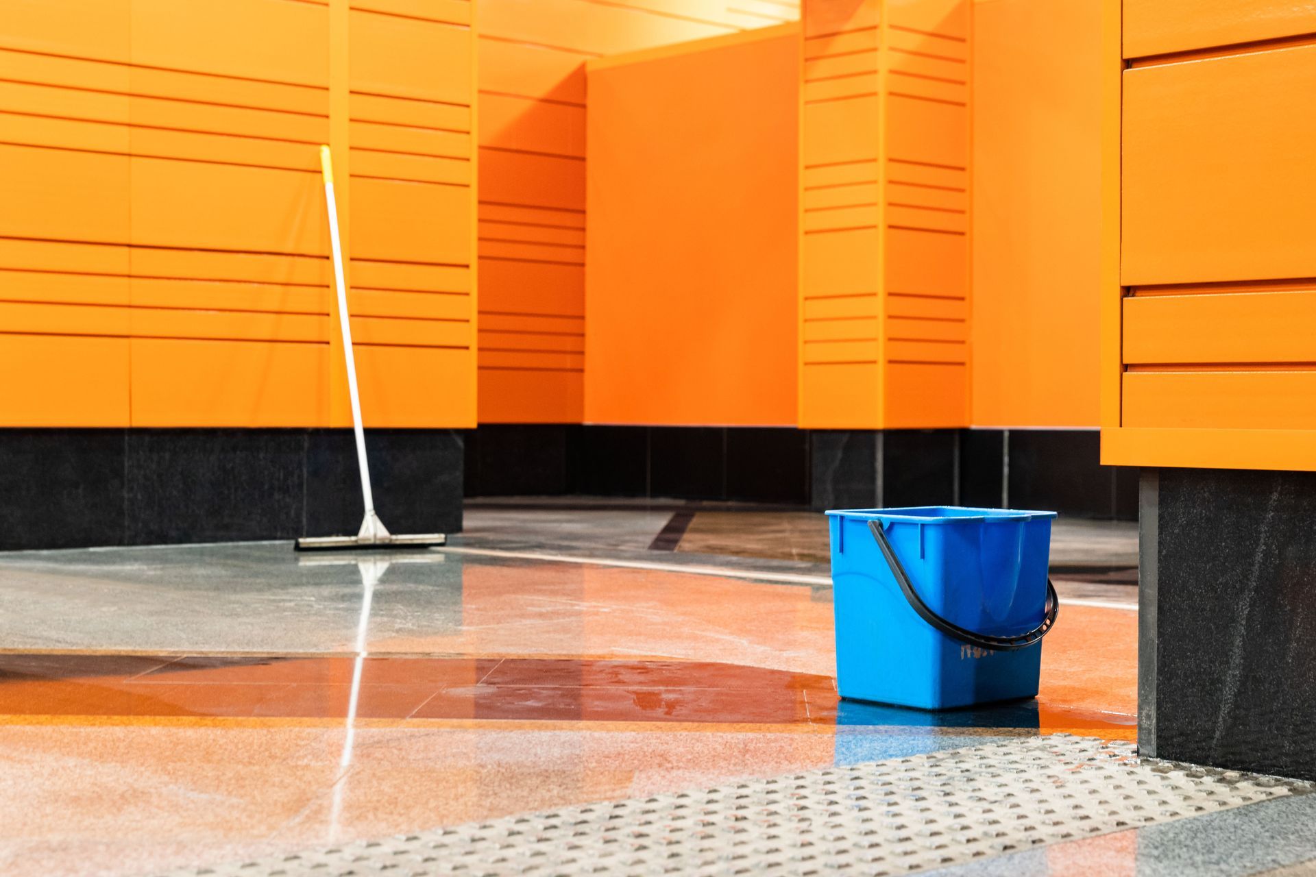 A blue bucket and mop are on the floor in front of an orange building.