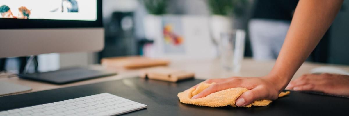 hand wiping down a desk around a desktop computer