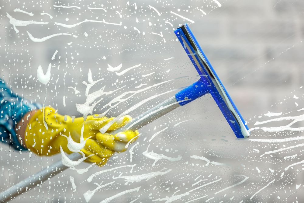 A person wearing yellow gloves is cleaning a window with a squeegee.