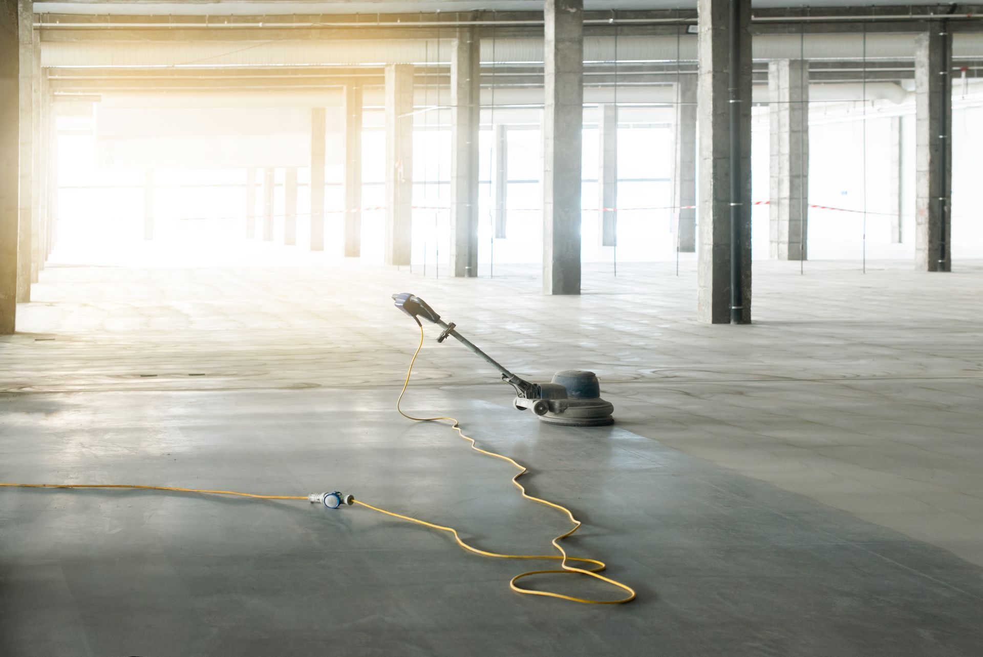 A concrete grinder is sitting on the floor of an empty warehouse.