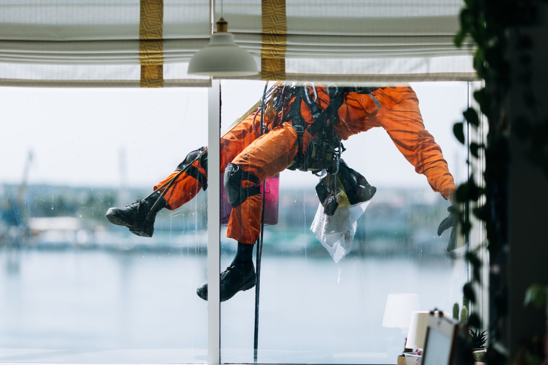 A man in an orange suit is hanging from the ceiling while cleaning a window.