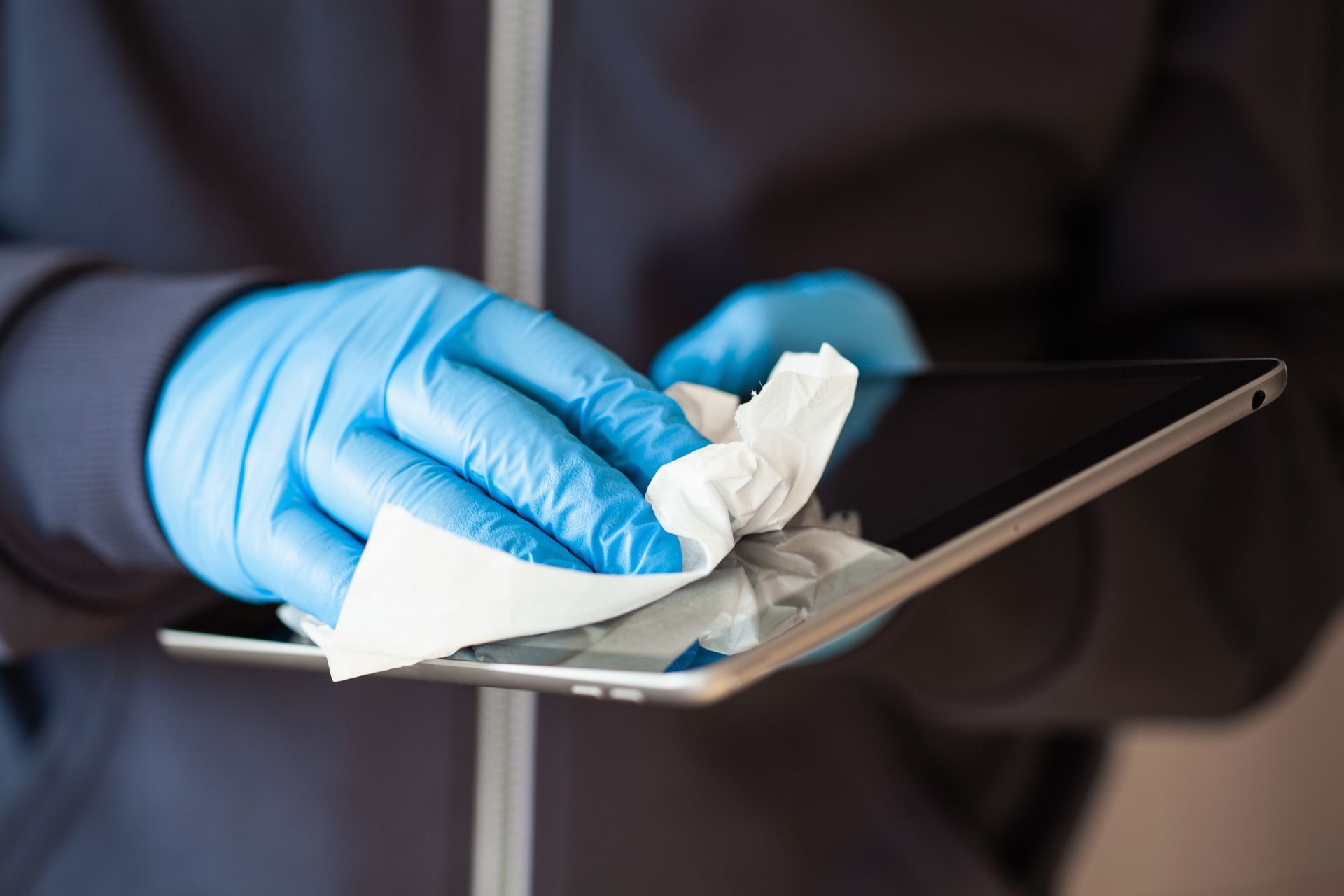 A person wearing blue gloves is cleaning a tablet with a napkin.