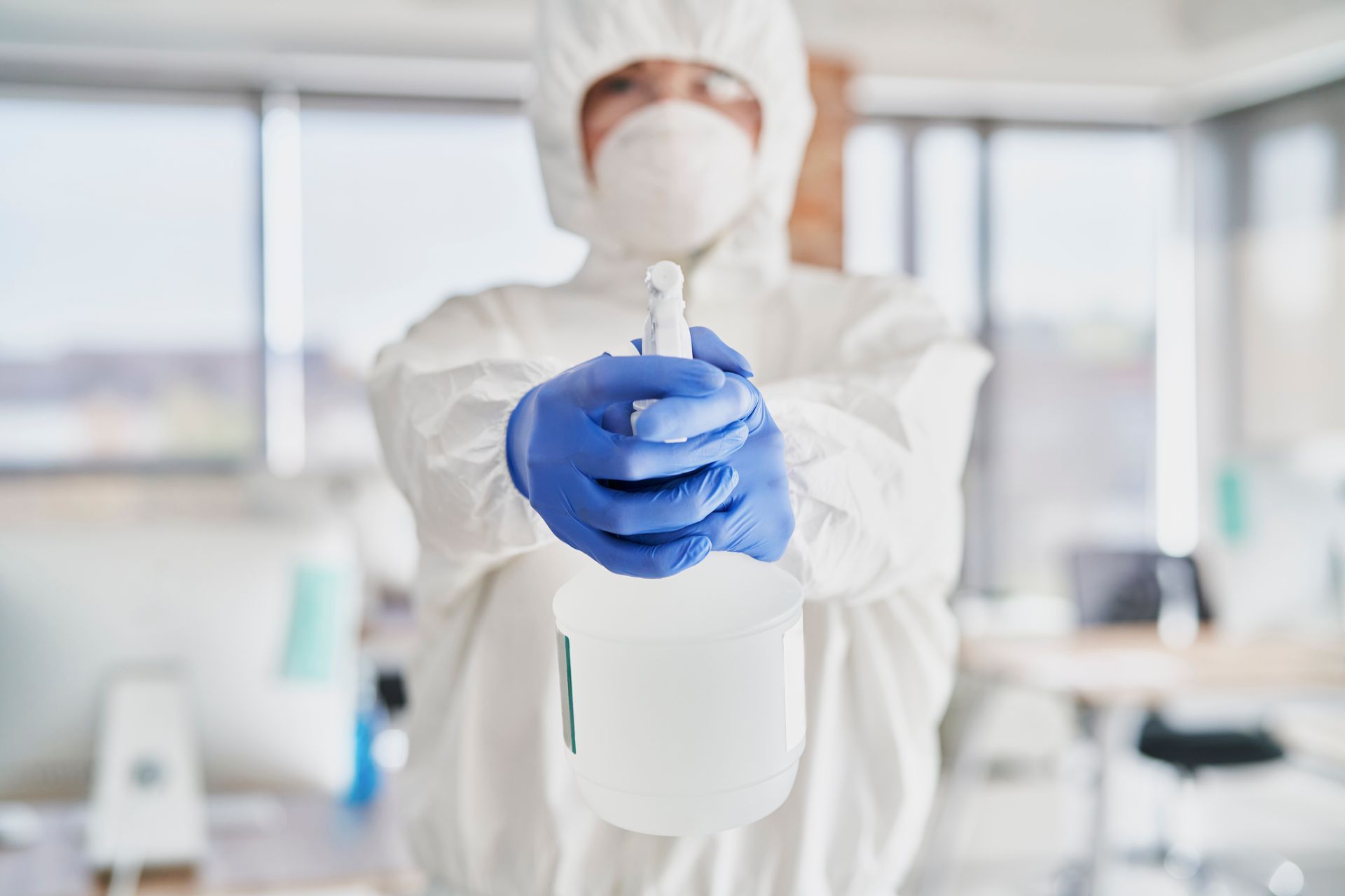 A man in a protective suit is holding a spray bottle.