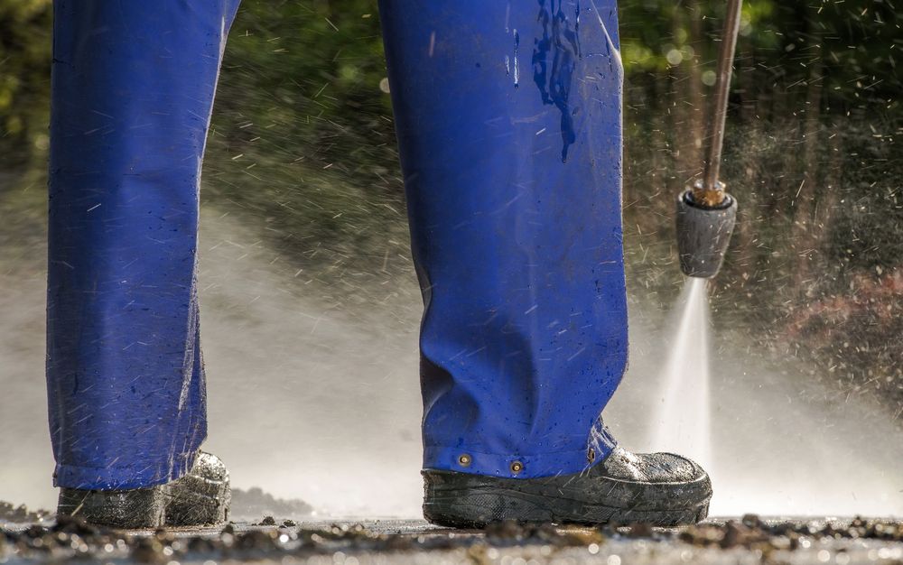 A person is using a high pressure washer to clean a sidewalk.