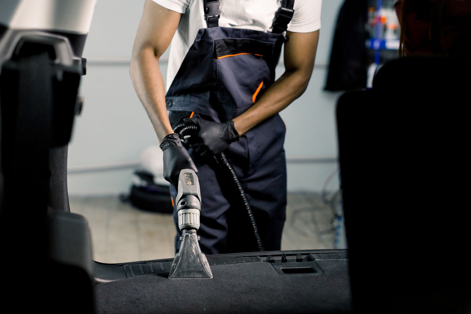 A man is cleaning the trunk of a car with a vacuum cleaner.