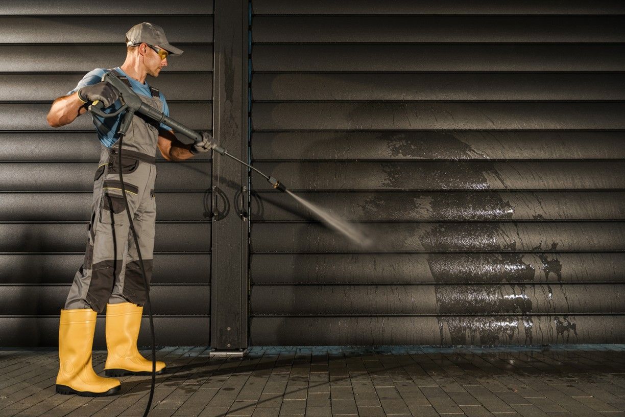 A man is using a high pressure washer to clean a garage door.