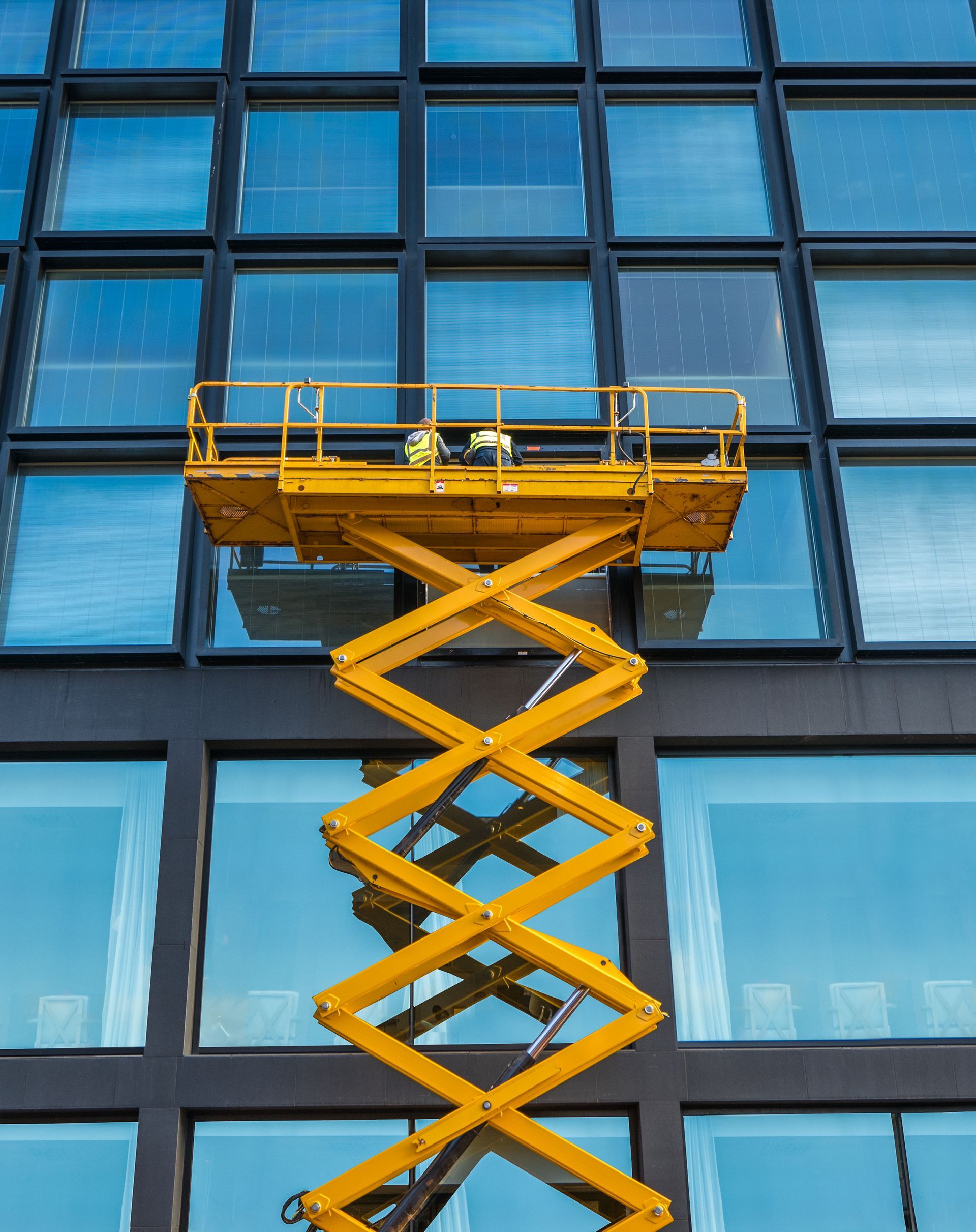 A man is standing on a yellow scissor lift in front of a building.