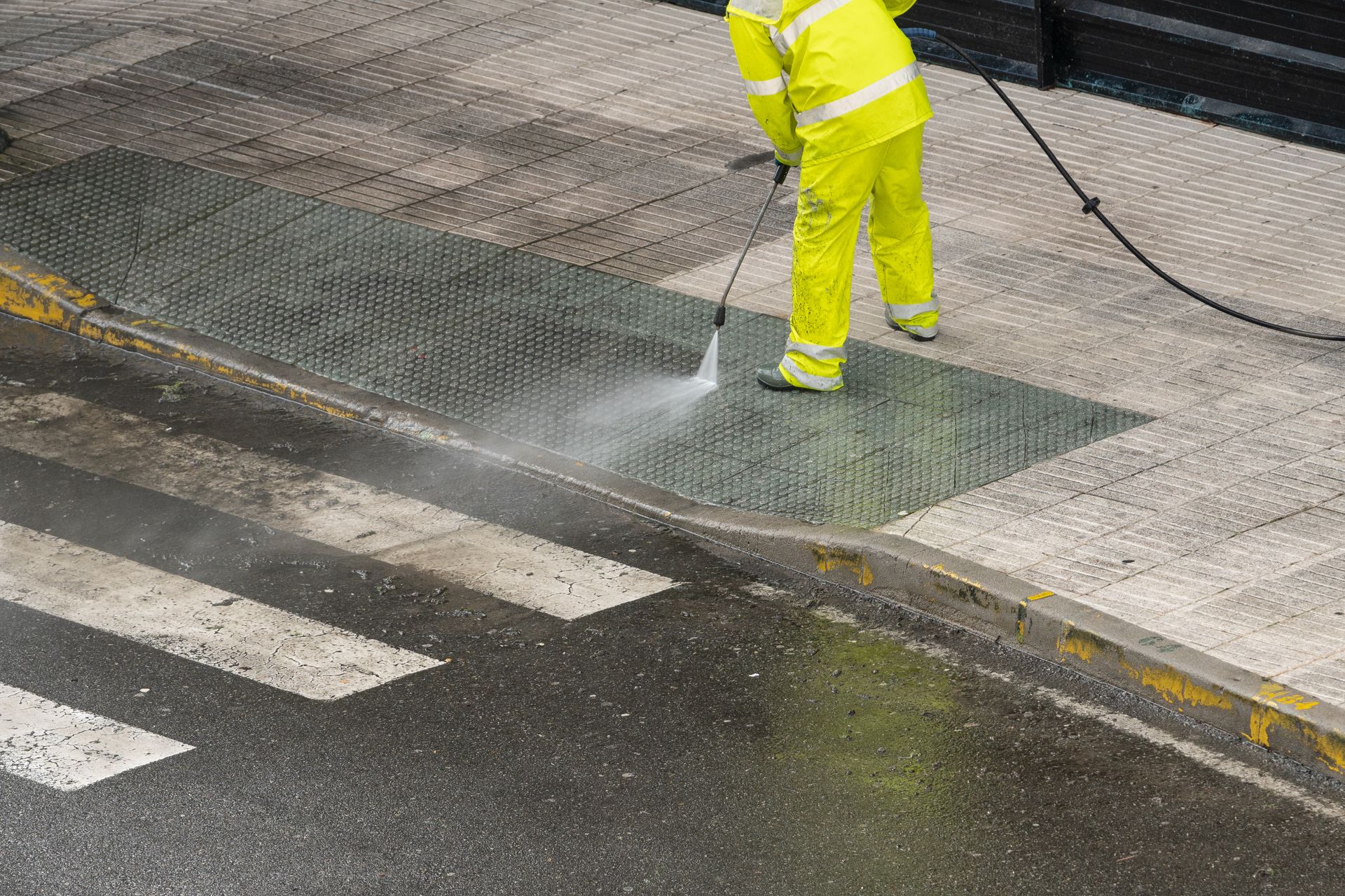 A man is cleaning the sidewalk with a high pressure washer.