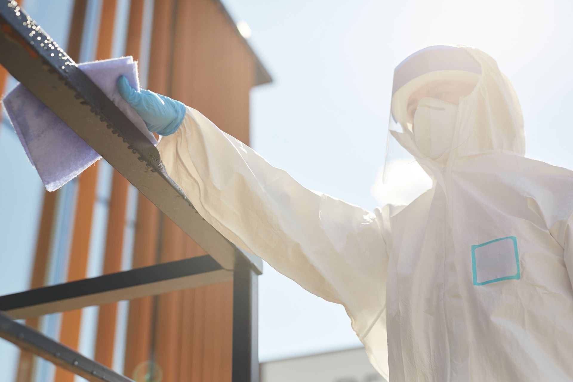 A man in a protective suit is cleaning a railing with a cloth.