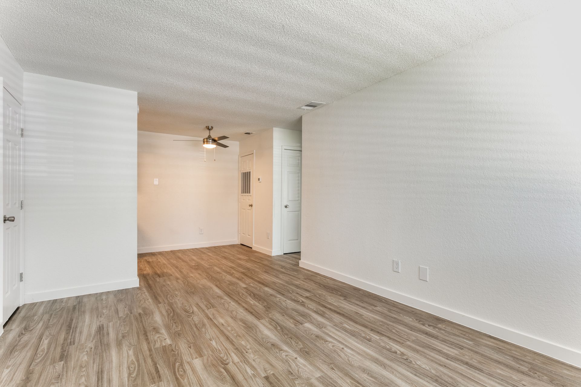 Empty apartment room with wood-look flooring, white walls, and a ceiling fan.