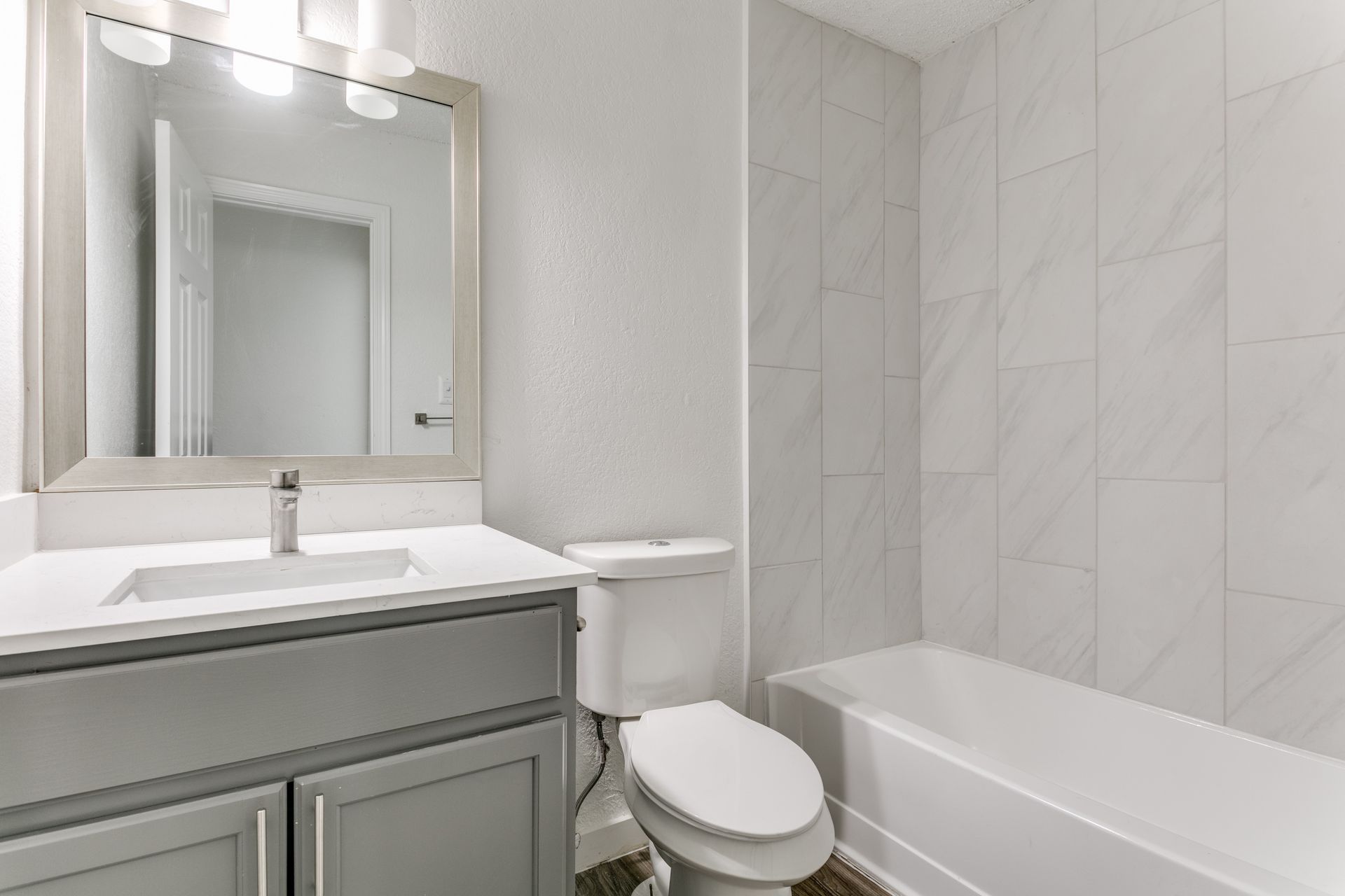 Gray-and-white bathroom with a vanity, toilet, and bathtub. The walls are tiled.
